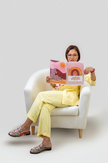 Woman in yellow suit reading a colorful booklet while sitting on a white armchair.