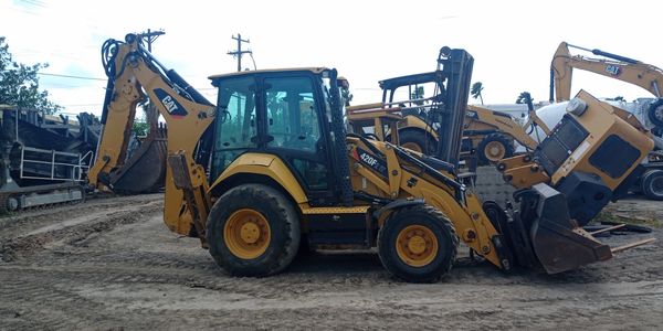 Yellow CAT backhoe loader parked on a dirt ground at a construction site.