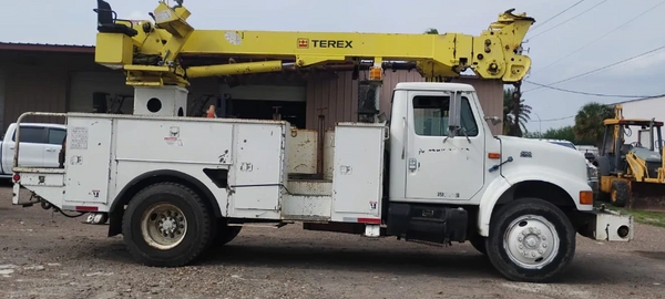 White utility truck with yellow Terex crane parked outdoors.