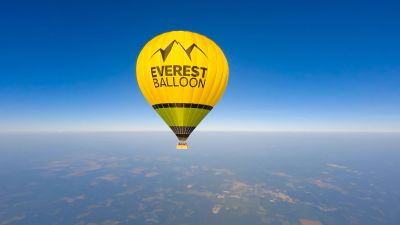 Bright yellow Everest hot air balloon floating high in clear blue sky.