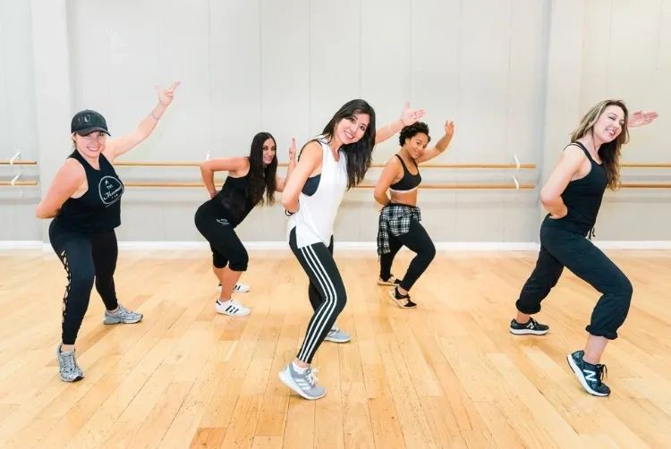 Five women in a dance studio posing mid-dance with smiles.