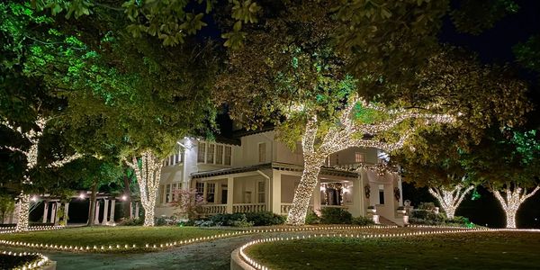 A beautifully lit house with trees wrapped in string lights at night.