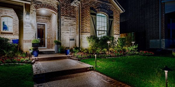 Well-lit brick house entrance with landscaped garden and pathway lights at dusk.
