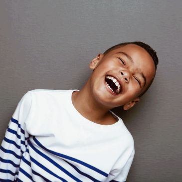Little boy laughing. Little boy is wearing a white sweater with blue horizontal stripes