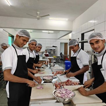 Chefs in a kitchen slicing onions together wearing aprons and hairnets.