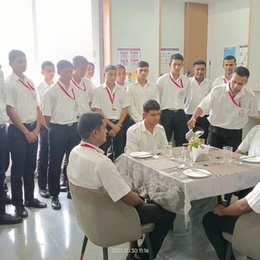 A group of young men in uniform gathered around a table with one serving water.