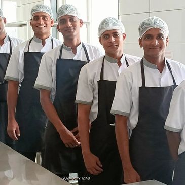 A line of chefs in white uniforms and black aprons standing in a kitchen.