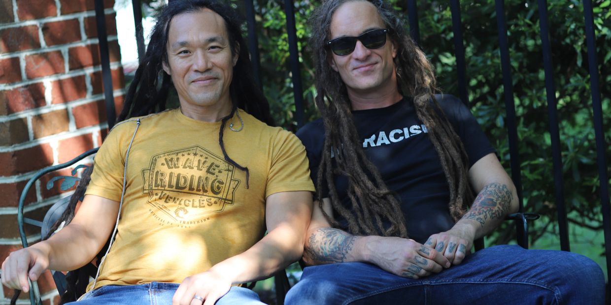 Jesse and Skanks sitting outdoors, one wearing a yellow shirt and the other a black shirt with sunglasses.