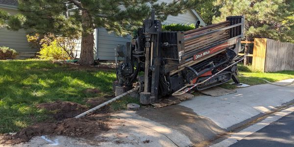 A Ditch Witch machine drilling underground near a residential sidewalk.