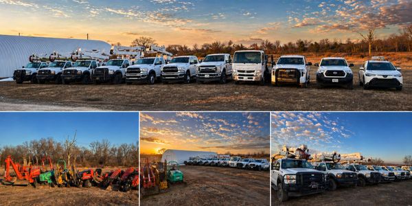 A fleet of utility trucks and construction equipment under a vibrant sky at sunset.