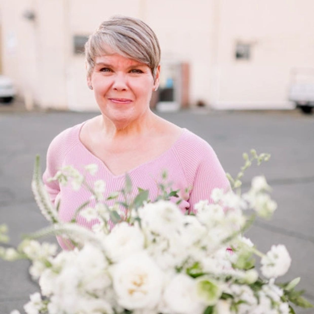 A smiling woman in a pink sweater with white flowers in front.