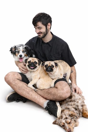 Young man sitting with three dogs and one dog lying down on a white background.