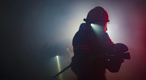 Firefighters with flashlights navigate a smoky, dark environment during a rescue mission.