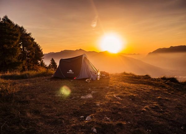 A tent set on a hill during a golden sunset with mountains in the background.