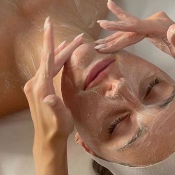 Woman applying facial mask with eyes closed.