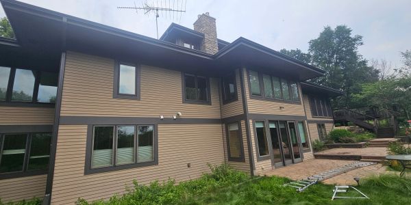 Modern two-story house with beige siding, dark trim, and multiple windows in a lush green setting.