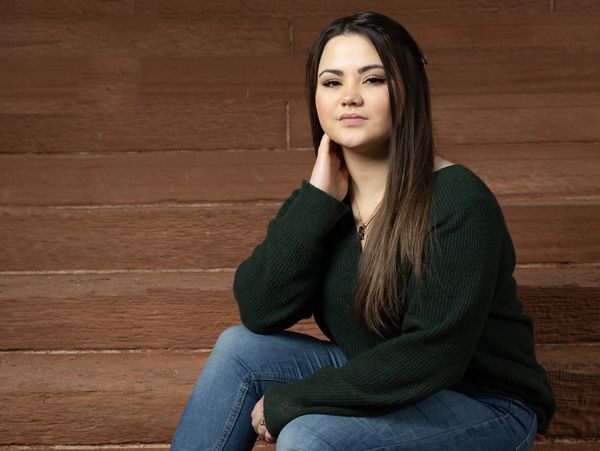 Young woman sitting on stone steps, wearing a green sweater and black boots.