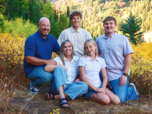 Smiling family posing outdoors in autumn scenery with colorful trees.