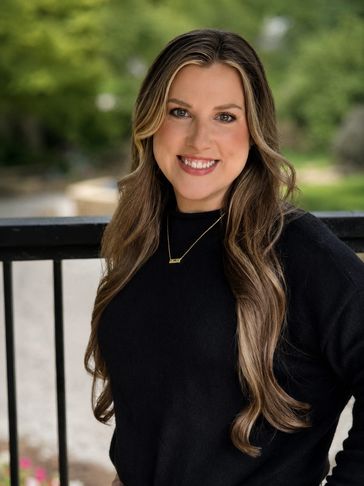 Smiling woman with long wavy hair in black sweater outdoors.