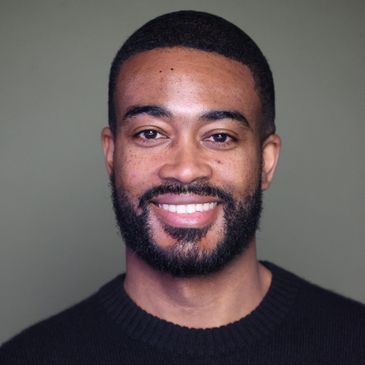 Smiling man with beard and short hair wearing a black sweater.