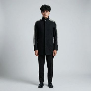 Young man in a black coat with checkered details and black pants.