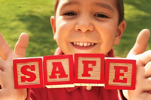 A young boy with a joyful expression holds up four red blocks spelling "SAFE"