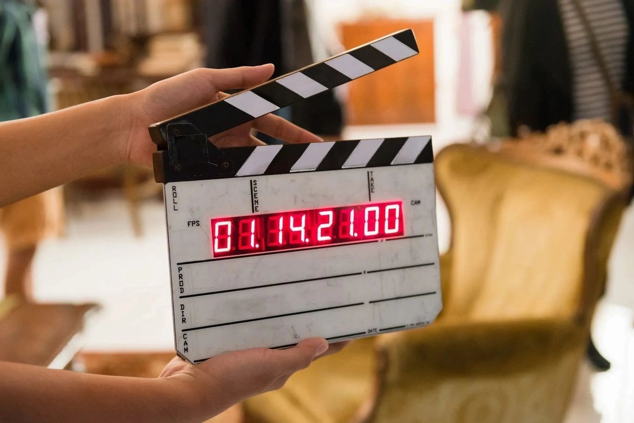 Hands holding a film clapperboard with digital time display.