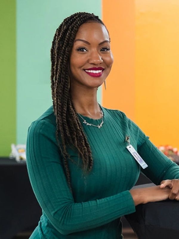 Smiling woman with braided hair wearing a green top indoors.