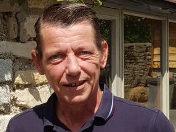 Middle-aged man smiling outdoors in front of a stone wall.