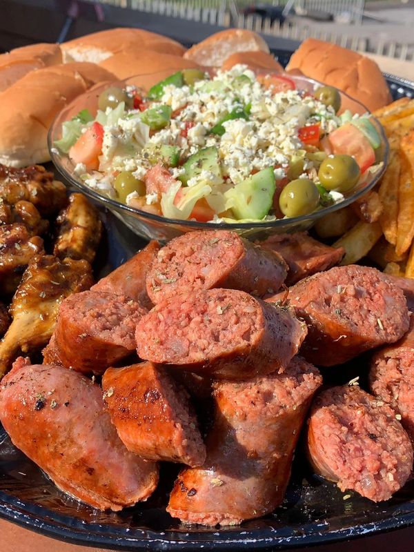 Grilled sausages with fresh salad, buns, and fries on a platter.
