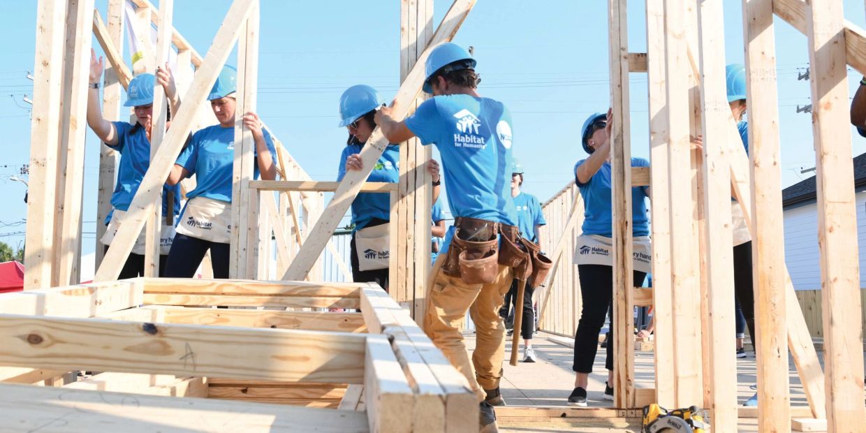 Volunteers building a wooden structure wearing blue Habitat for Humanity shirts.