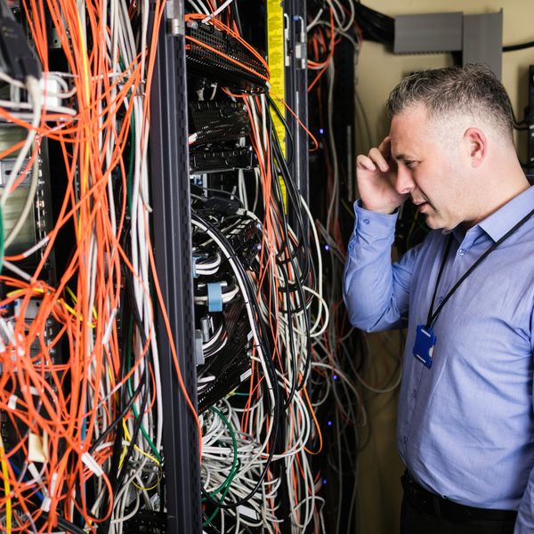 Confused man standing in front of messy data rack with patch cables mixed and twisted.