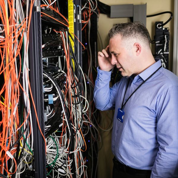 Technician frustrated at data rack with bunches of messy patch cables and network equipment.