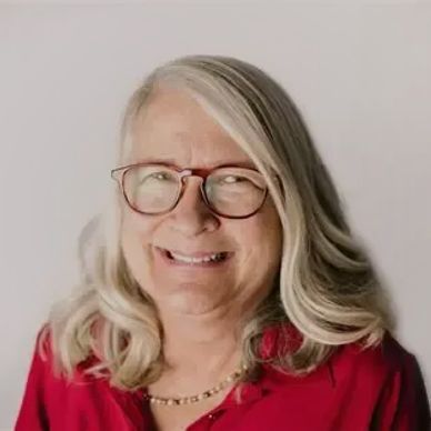 Smiling elderly woman with glasses and gray hair wearing a red shirt.