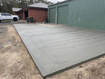 Shed apron outside a green shed next to a house.