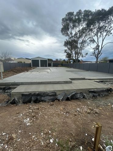House slab with a shed in the background and trees and a fence