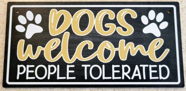 A humorous sign saying dogs welcome, people tolerated, with paw prints.
