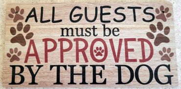 Wooden sign stating guests must be approved by the dog with paw prints.