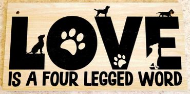Wooden sign saying "LOVE is a four legged word" with dog silhouettes and paw prints.