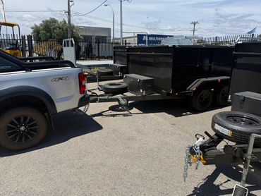 Silver 4x4 truck towing a large black trailer in a parking lot.
