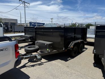 Black utility trailer hitched to a white 4x4 vehicle in a parking lot.