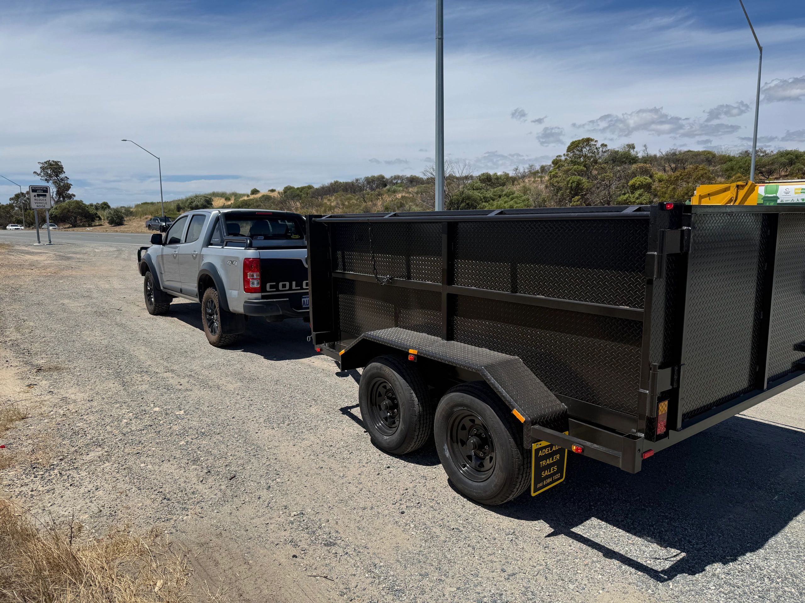 Silver pickup truck towing a large black trailer on a sunny roadside.