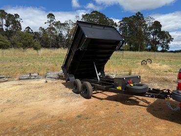 A black trailer with a raised bed attached to a vehicle in a rural area.