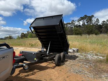 A black dump trailer hitched to a white 4x4 truck in a rural area.