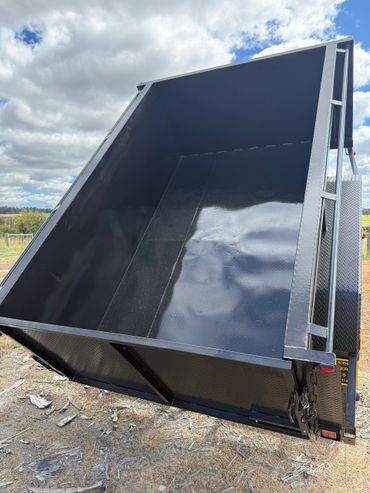 Empty black metal trailer bed under a cloudy sky.