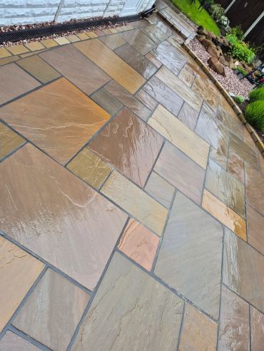 Wet multicolored stone tiles arranged in a patio pattern.