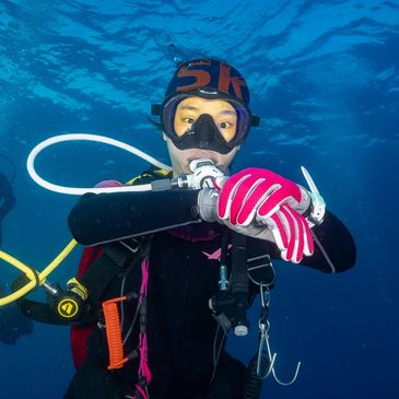 Scuba diver underwater checking wrist gear in clear blue ocean.