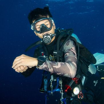 Scuba diver underwater wearing full gear and a camouflage wetsuit.