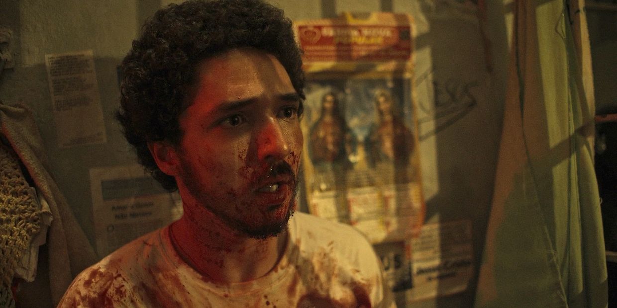 Man with blood on his face looks shocked in a dimly lit room.