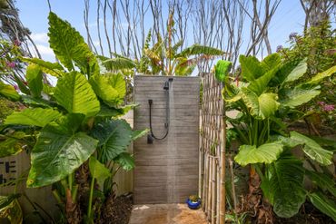 Outdoor shower surrounded by lush green plants and bamboo fencing.